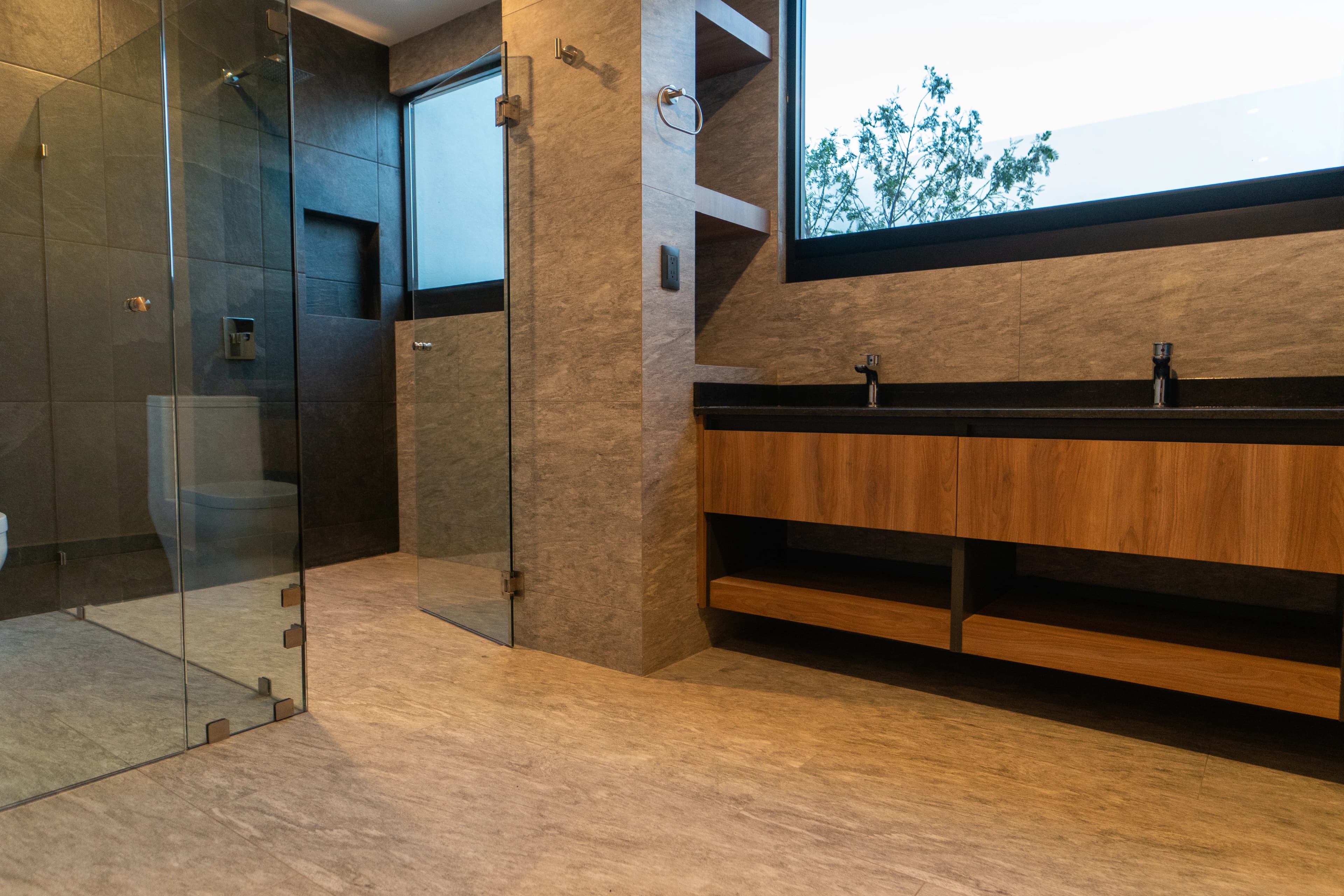 Baño de Casa Cointzio con regadera de cristal y mueble de madera sobre piso de piedra