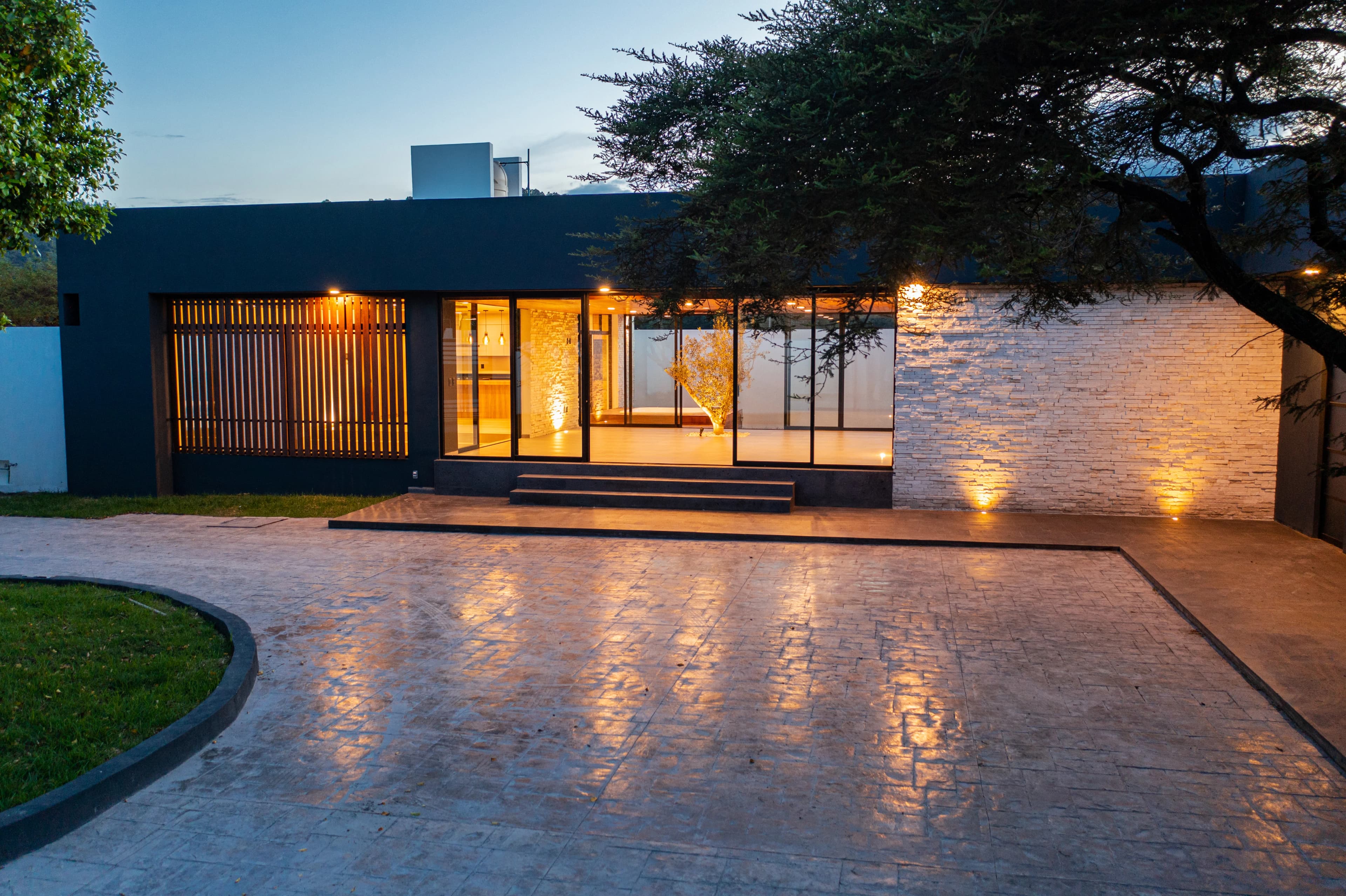 Acceso iluminado de Casa Cointzio al anochecer, con muro de piedra y celosía