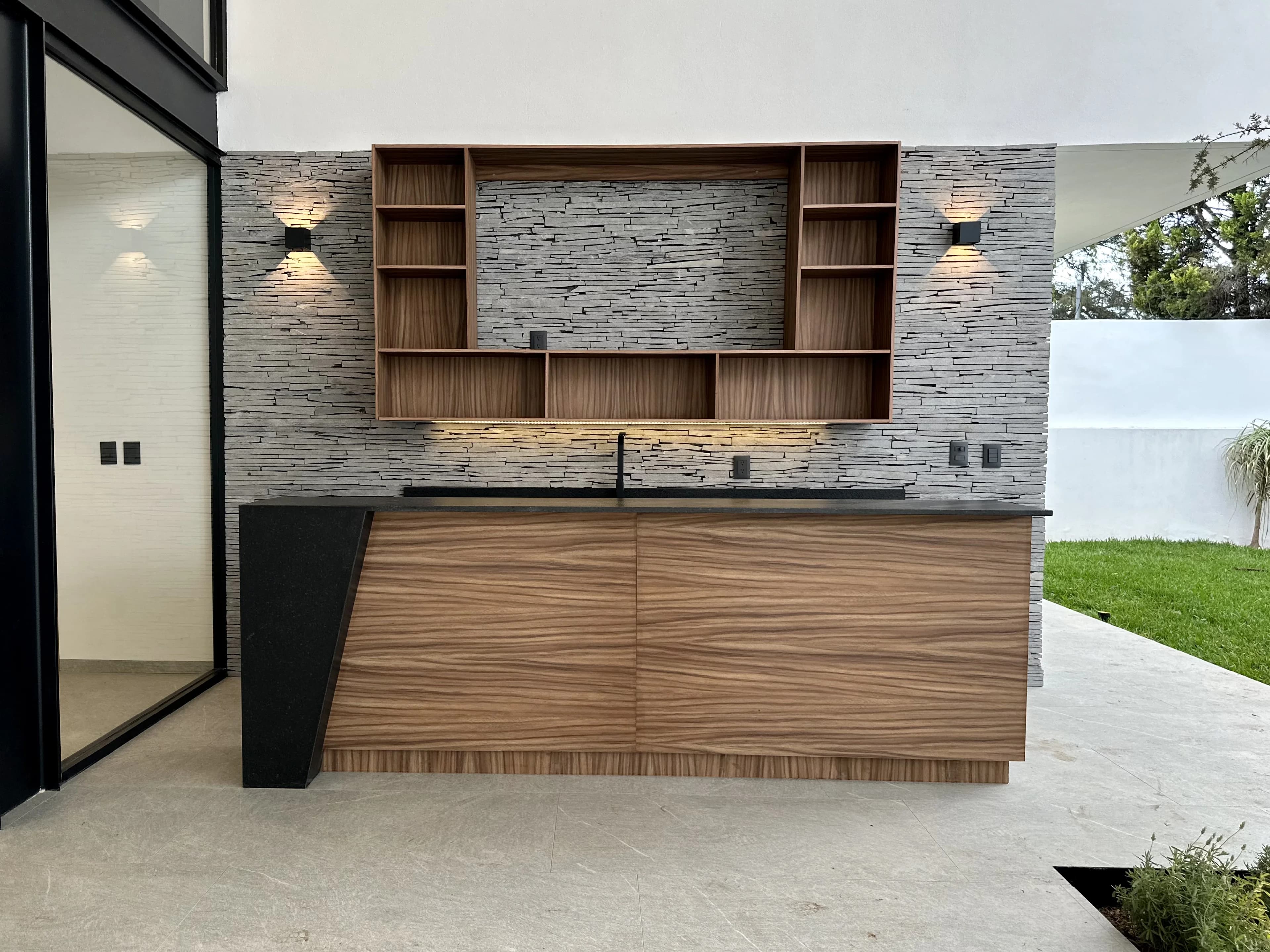 Asador de Casa del Ángel con muro de piedra laja y barra de madera abierta al jardín