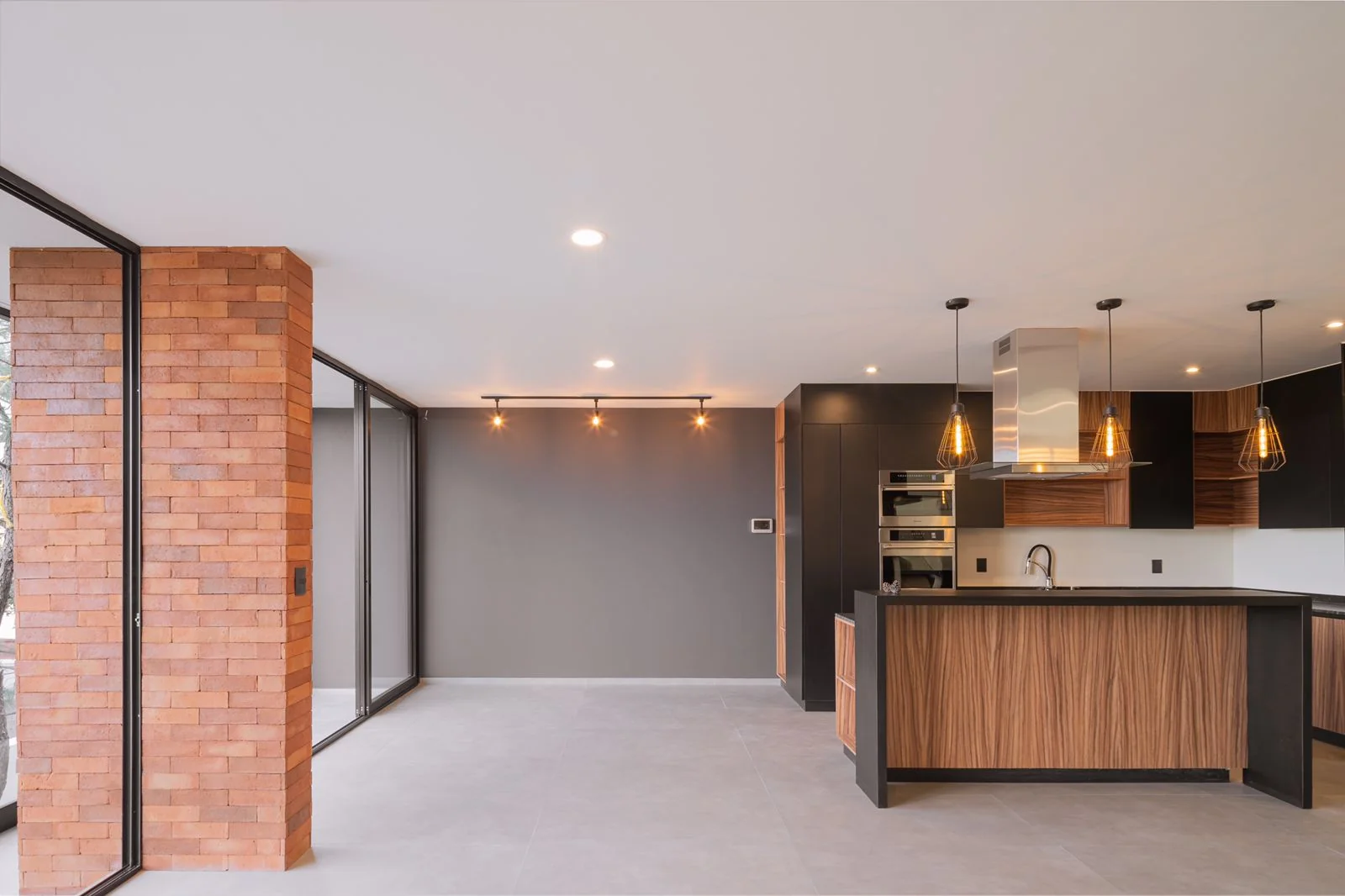 Estancia de Casa Dos Pinos con muro de ladrillo aparente y la cocina al fondo