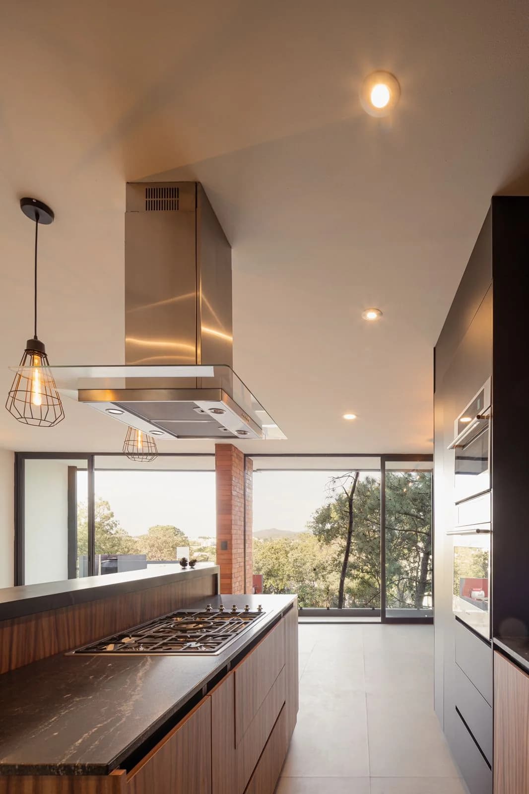 Cocina de Casa Dos Pinos con isla, campana de acero y ventanal al bosque