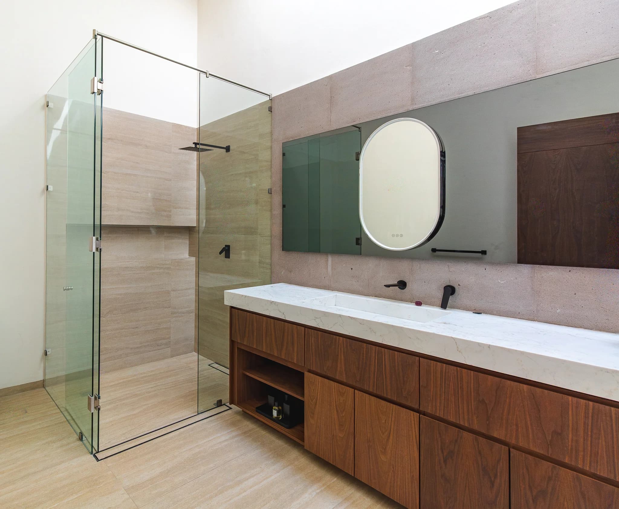 Baño de L&C con regadera de cristal, mueble flotante de madera y espejo ovalado