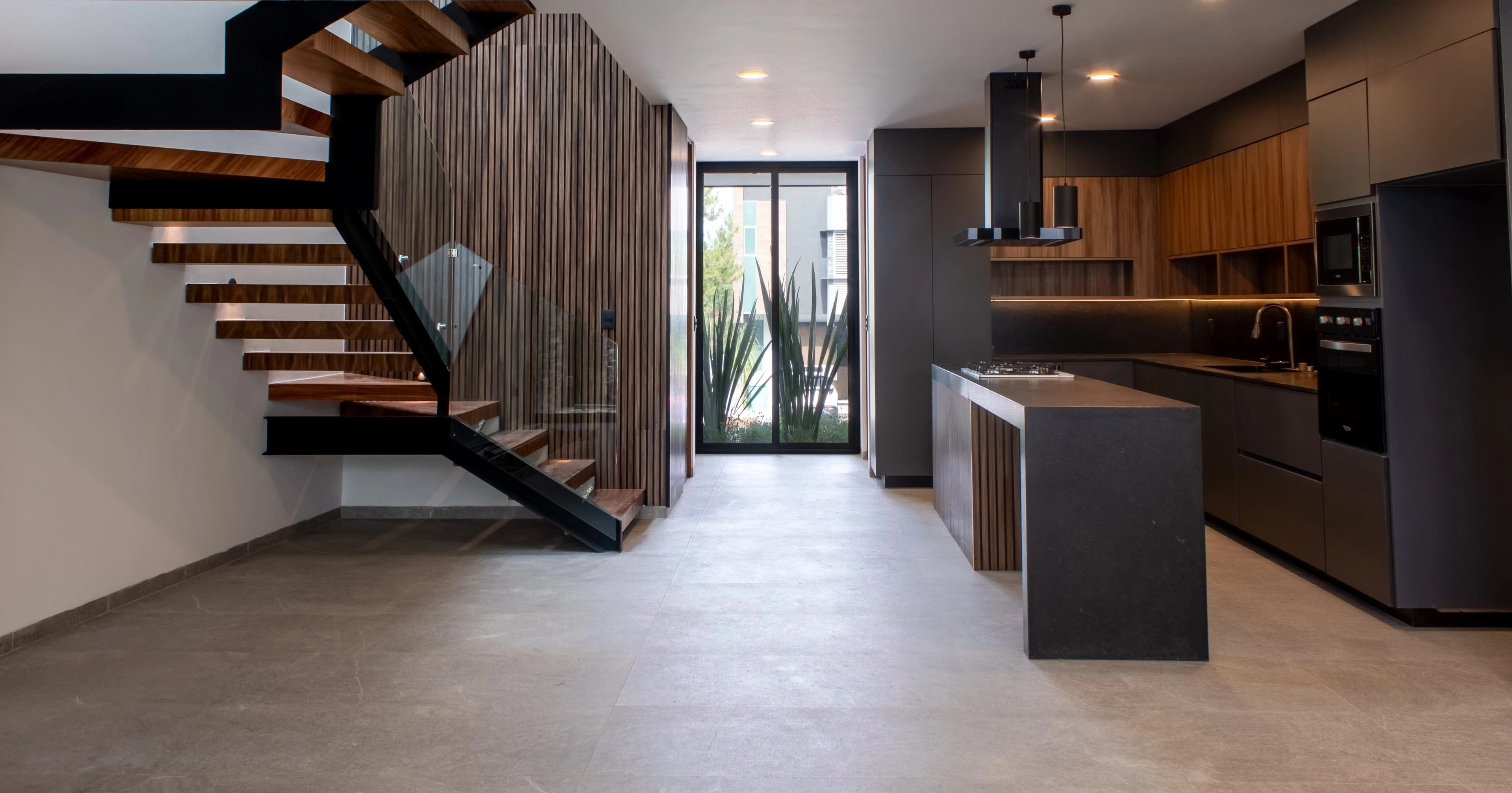 Escalera de Casa Encinos con peldaños de madera y muro de duela, junto a la cocina